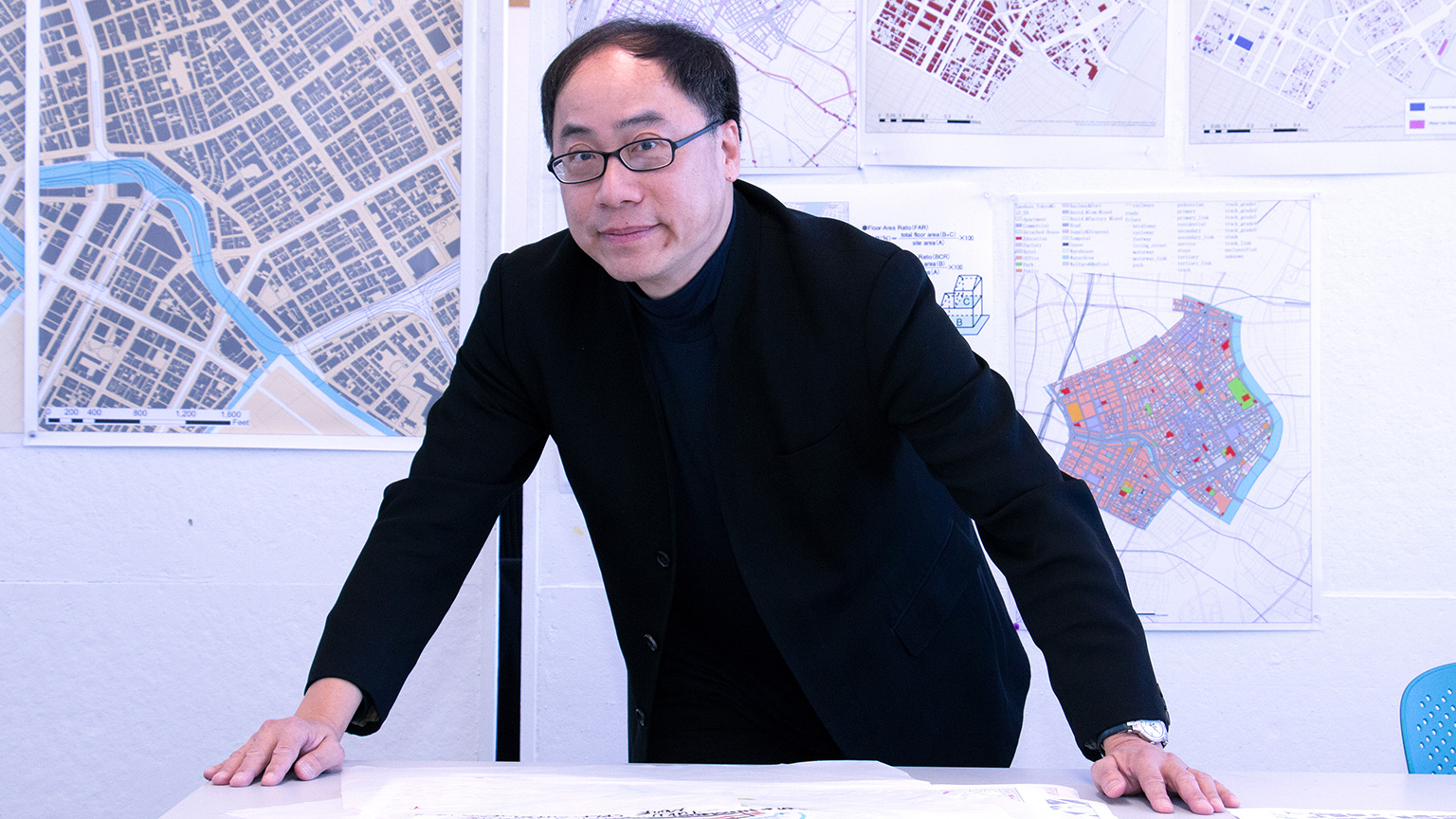 Perry Yang leaning on a table in front of Tokyo Smart City studio designs