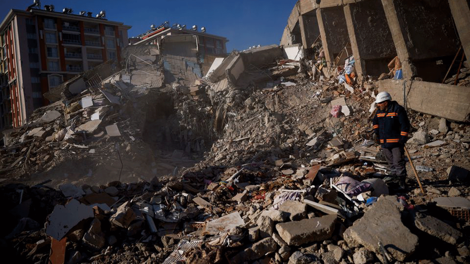 Man in safety gear examines a rubble of a collapsed building