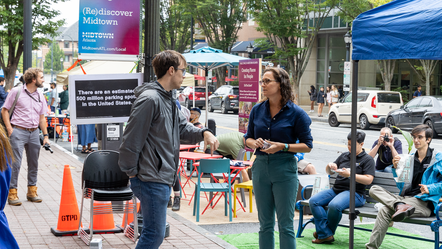 A representative from MARTA talks to a pedestrian in front of a parklet with benches and artificial turf created by the MARTA team.