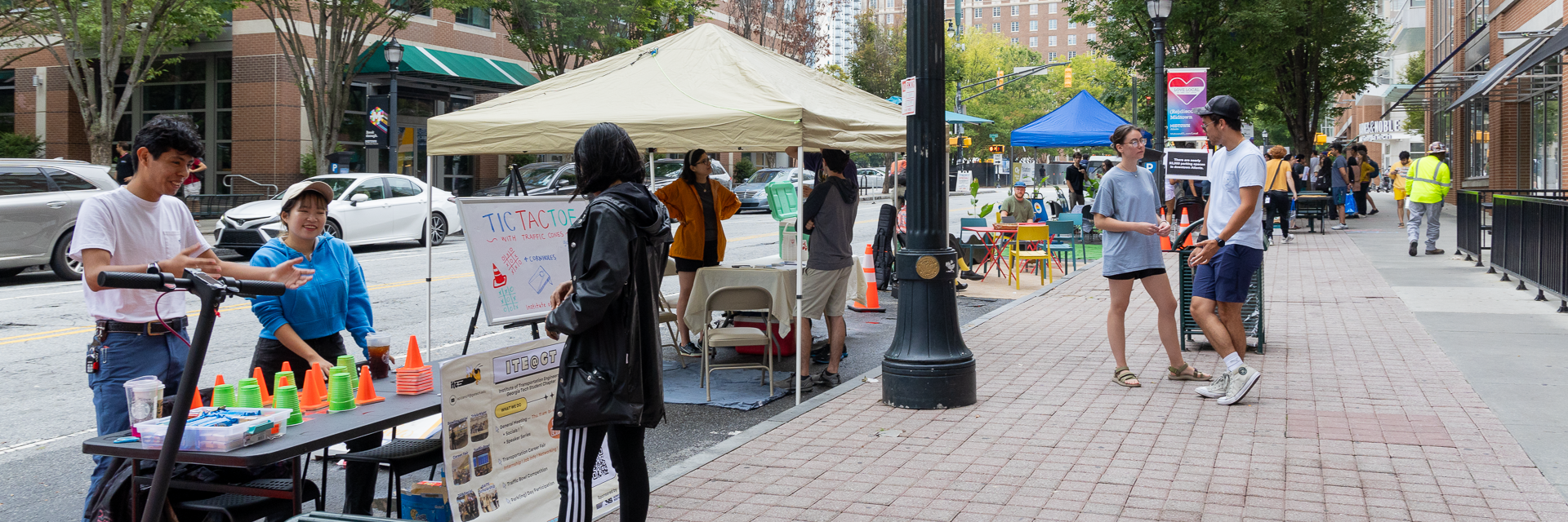 View down sidewalk showing street parking occupied by tents and informational tables